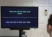 photograph showing the back of a person's head who appears to be an adult with short brown hair. They are gazing at an electronic screen that reads 'Then how did he know your name'.